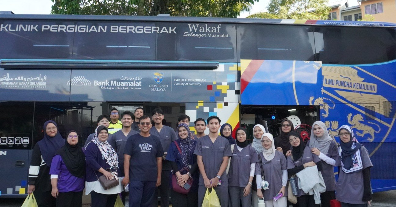 Sukarelawan UM bersama komuniti yang terlibat dalam pengajuran program di hadapan bas klinik bergerak pergigian